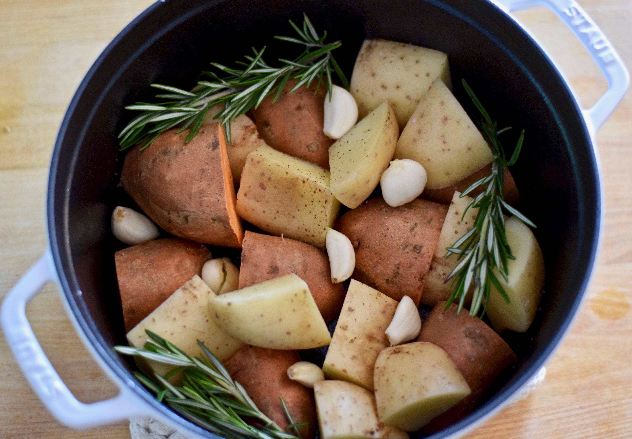 chopped sweet and gold potatoes with rosemary and garlic in dutch oven