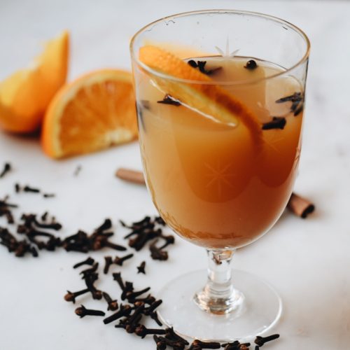 mulled cider surrounded with cloves, oranges, and cinnamon sticks