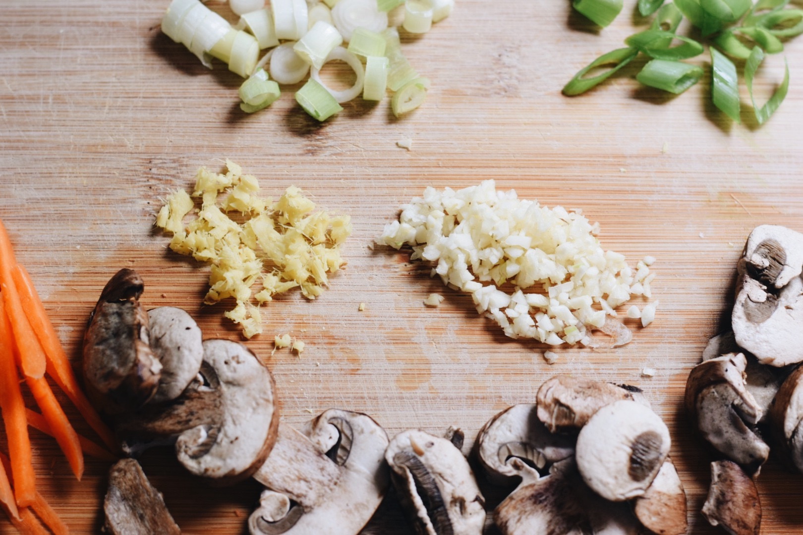 mushrooms, garlic, ginger, green onions, and carrots on a cutting board