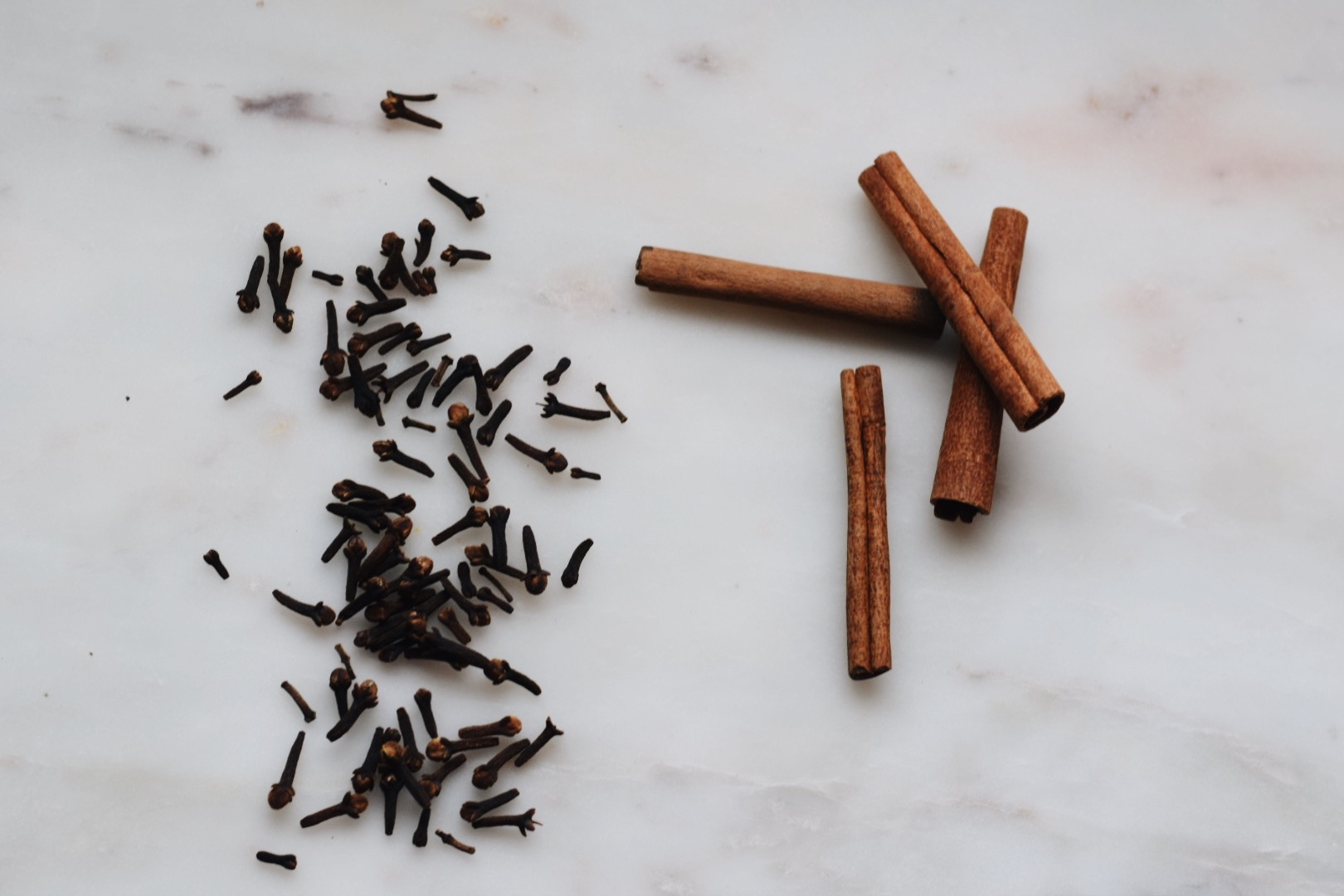 whole cloves and cinnamon sticks on a white surface