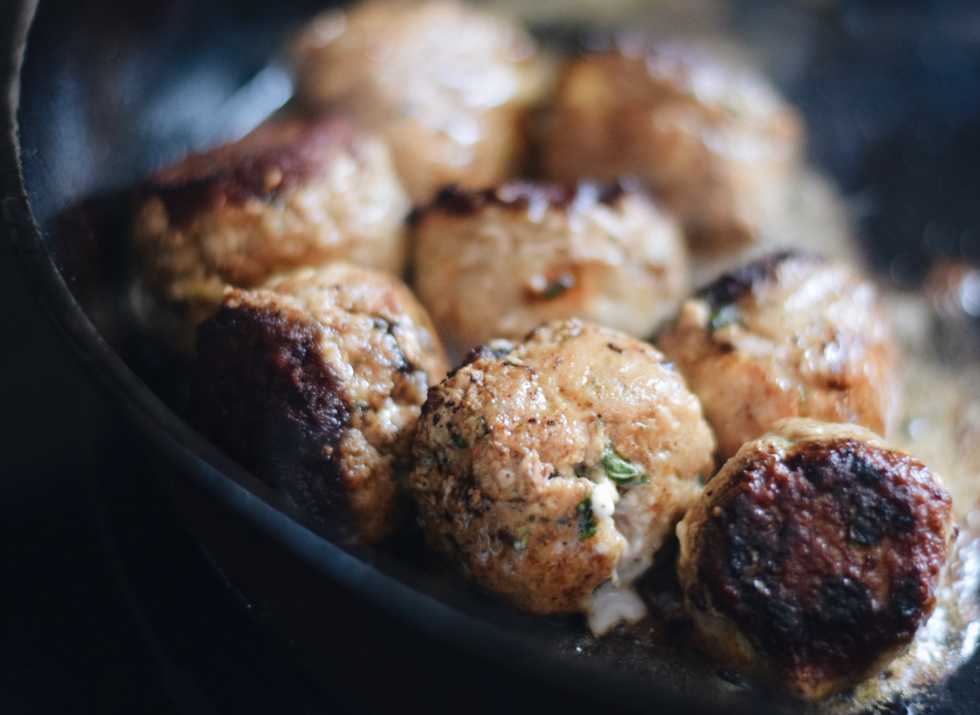 meatballs cooking in an iron skillet