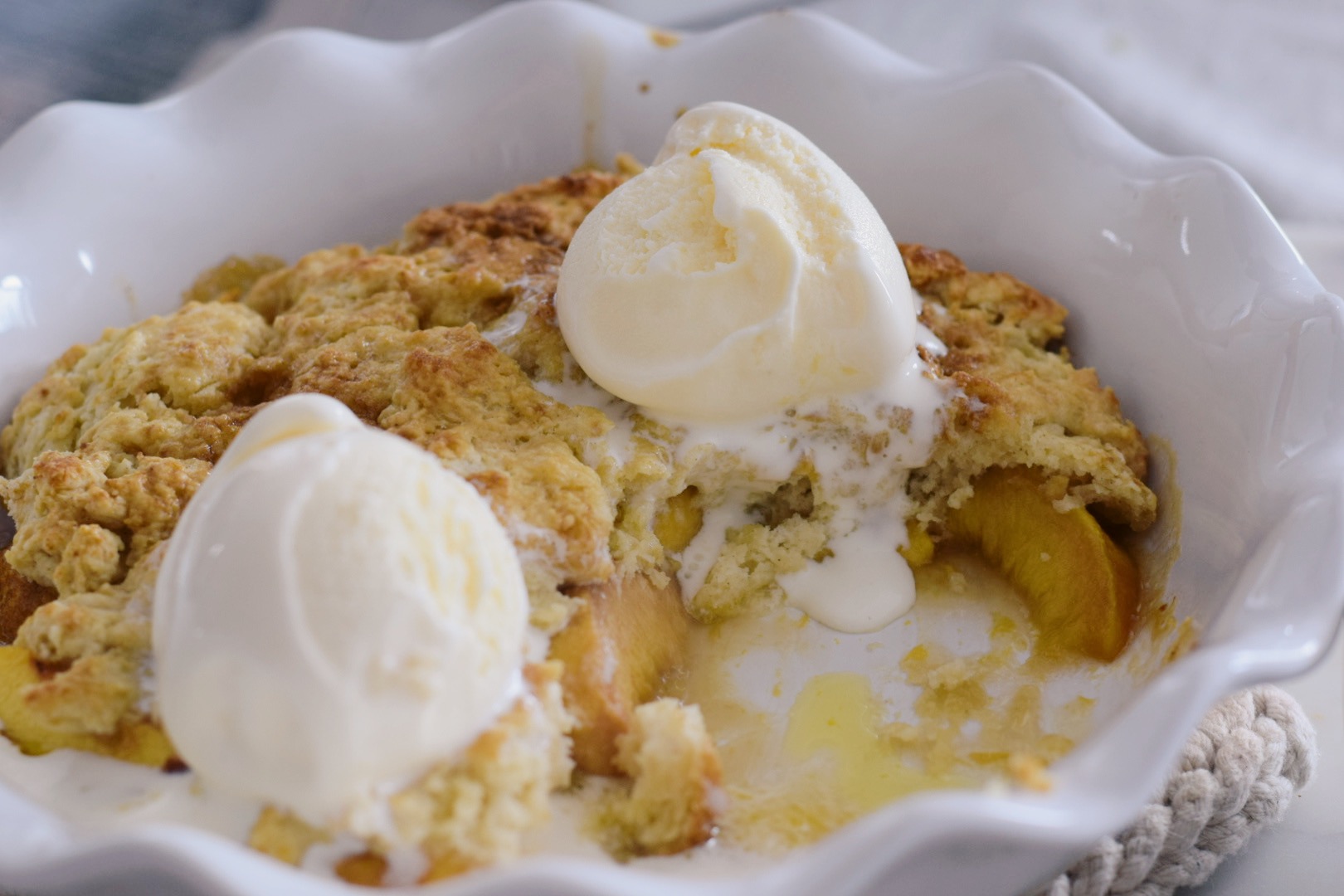 biscuit-top peach cobbler in a pie dish with ice cream